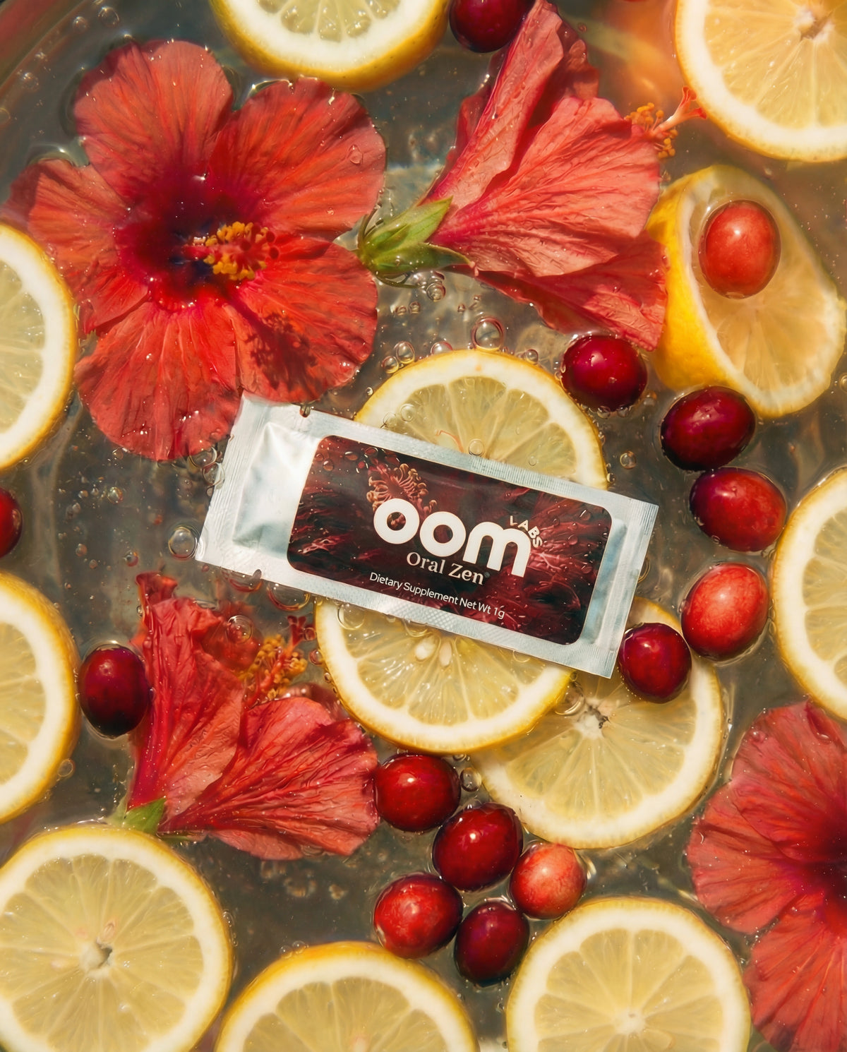 Oral Zen gag reflex control sachet floating in water with its natural ingredients — lemon slices, cranberries, and hibiscus flowers. There is an editorial vogue style to the image.