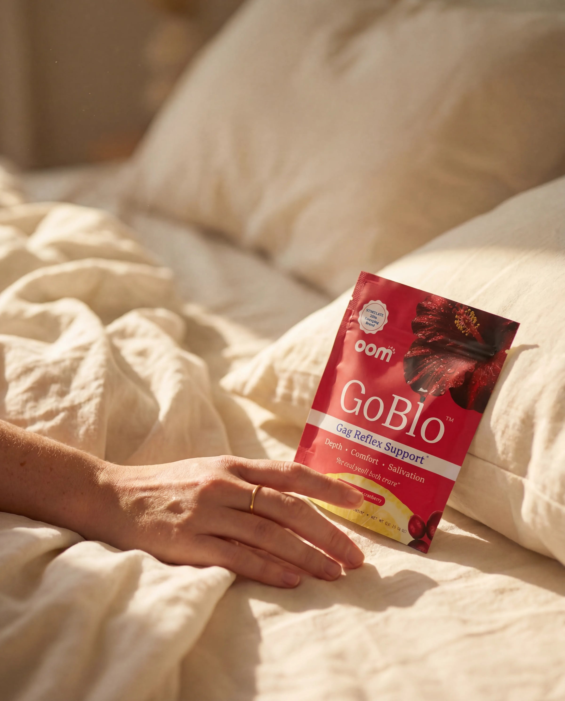 A hand reaching for a GoBlo stick pack on a bed