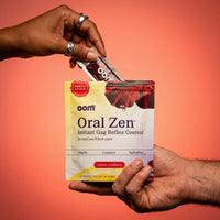 One black female hand with silver jewelry in the upper left pulls Oral Zen gag reflex control sachet from the pouch against a bold coral red background. A masculine male hand holds the multi-pouch from the bottom right of the screen. Edges of image have darker coral color.