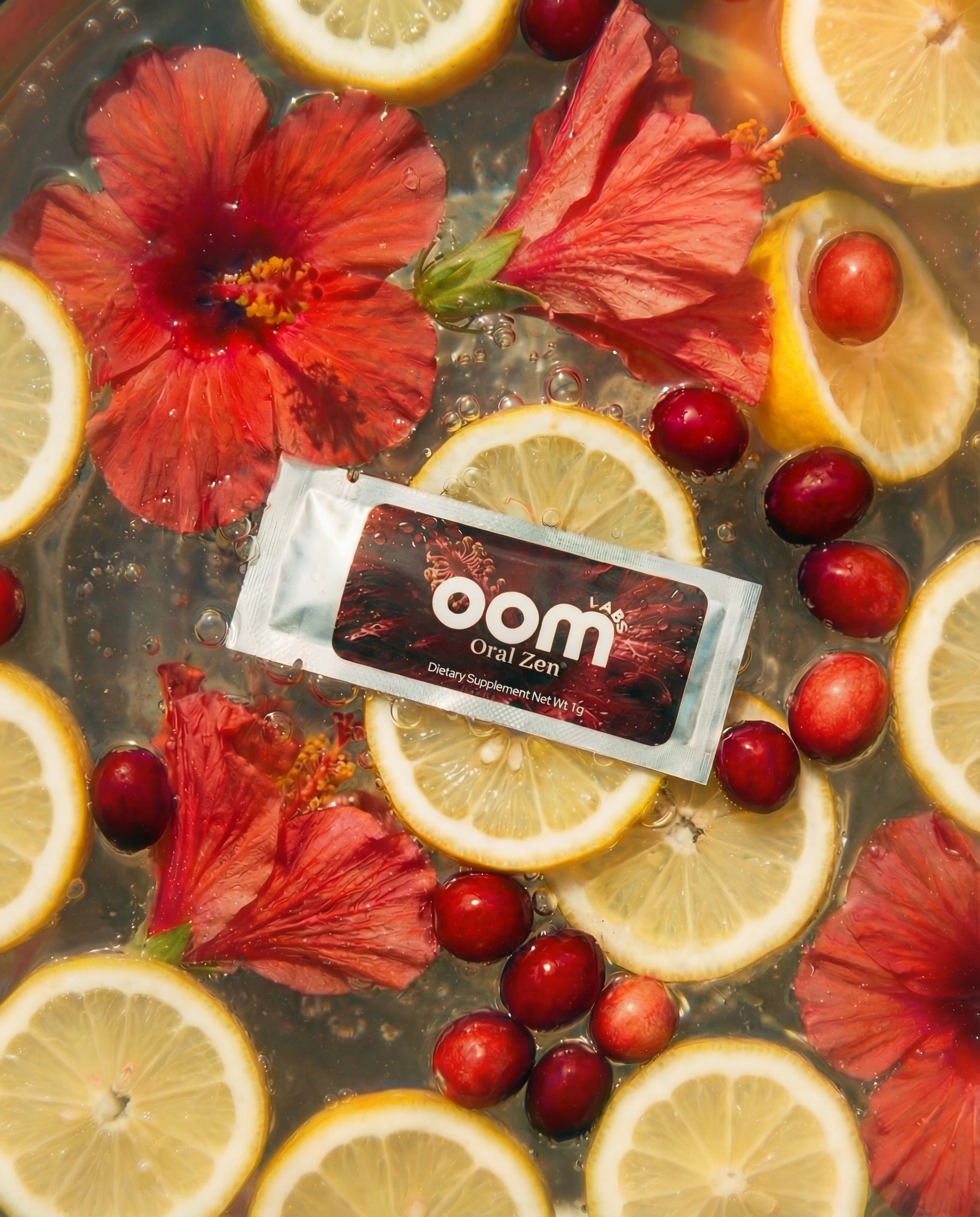 Oral Zen gag reflex control sachet floating in water with its natural ingredients — lemon slices, cranberries, and hibiscus flowers. There is an editorial vogue style to the image. 